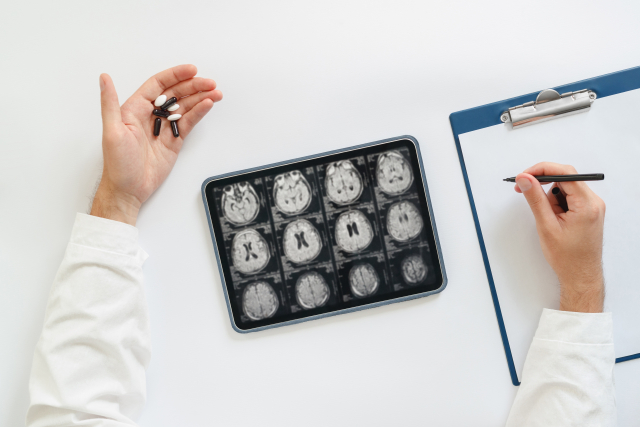 薬の入った手のひら 脳の検査画像が表示されたタブレット メモを取る手