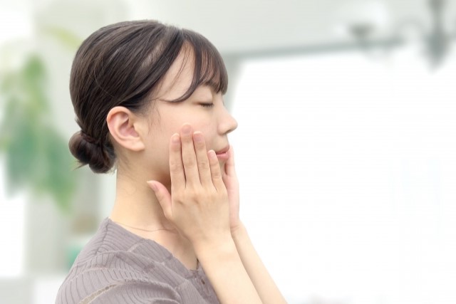 目を閉じ両手で頬を優しく押さえる女性