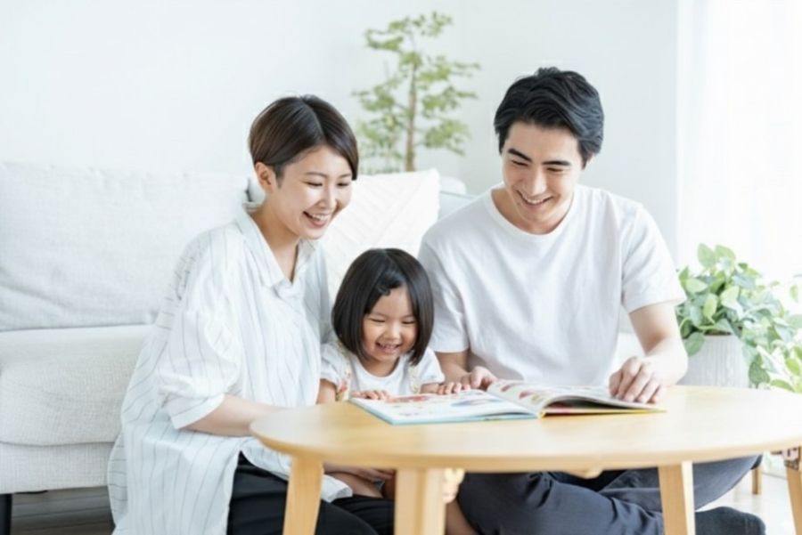 笑顔の家族3人がリビングで絵本を読む