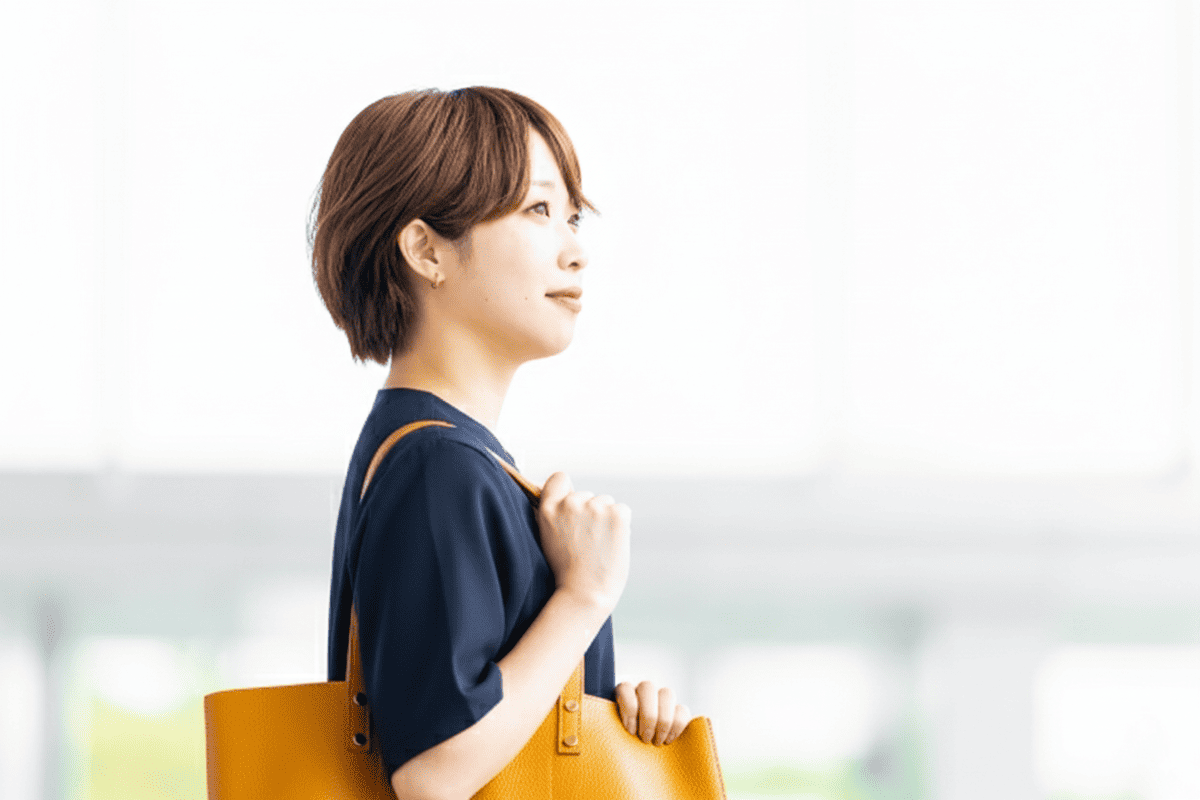ショートカットの女性が黄色のトートバッグを肩にかけて上を見ている