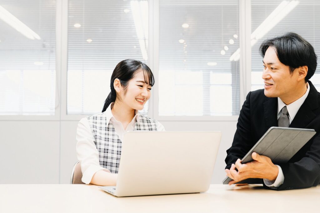 ノートパソコンとタブレットを前に笑顔で話す男女