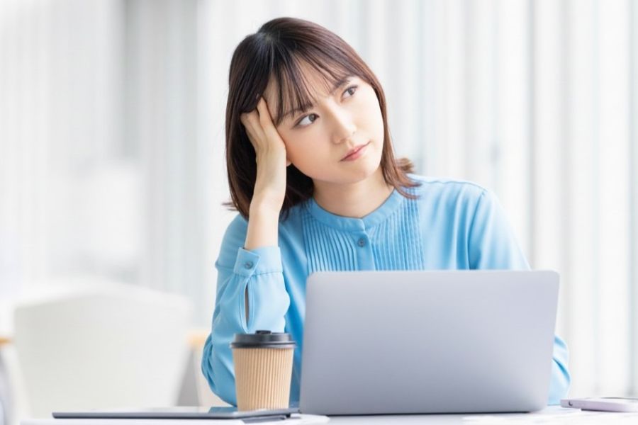 ノートパソコンの前で頬杖をついて考え込む女性